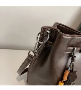 Détail d'un sac seau en cuir marron foncé avec crochet gris fusil et pompon décoratif