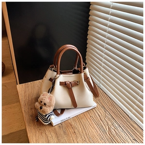 Détail du sac seau en cuir crème avec poignées marron et pendentif ours en peluche