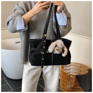 Detail of black suede tote bag with white contrast stitching and plush bunny pendant