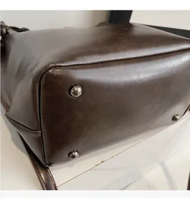 Détail de la base du sac seau en cuir marron avec pieds en métal et surpiqûres soignées