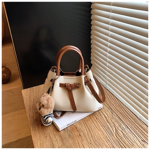 Détail du sac seau bicolore crème et marron avec breloque ours sur un bureau en bois
