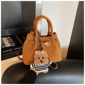 Détail d'un sac seau marron avec une peluche d'ours et des boucles métalliques dorées