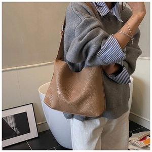 Close-up of caramel pebbled leather tote bag showing drape and texture on a model