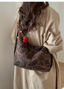 Detail of vintage paisley print tote bag with red pompom charm shown on model's shoulder