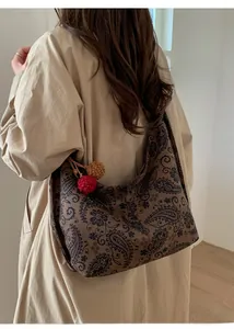 Close-up of vintage paisley tote bag with decorative plush charms on a model shoulder