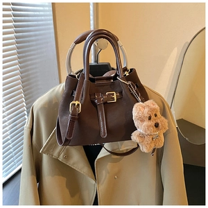 Détails d'un sac à main vintage marron foncé avec boucles dorées et pendentif chien en peluche