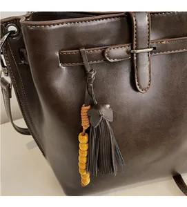 Détail du sac cabas en cuir marron foncé avec pompon et perles en bois sur le côté latéral