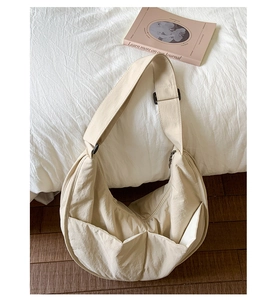 Detail of beige nylon half-moon bag with wide adjustable strap on a minimalist bed