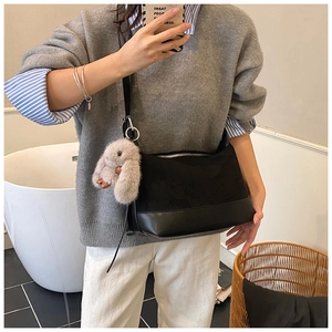 Detail of black pleated crossbody bag with a cute plush rabbit pendant charm on the strap