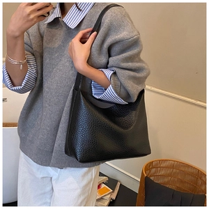 Close-up of litchi grain leather texture on a black hobo shoulder bag with wide strap