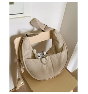 Detail of beige nylon crescent bag with wide strap and cute plush bear charm on a chair