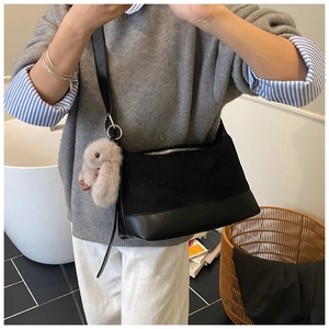 Detalle de bolso tote negro bimaterial con correas de cuero y colgante de conejo de peluche