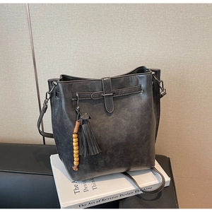 Détail du sac seau gris mat avec perles en bois et pendentif à pompon en cuir élégant