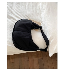 Detail of a large black nylon crescent bag with quilted texture on a white bed surface