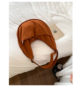 Detail of caramel nylon crescent bag with wide strap on a minimalist white bedding