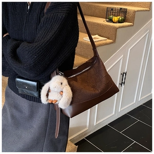 Detail of dark brown pleated hobo bag featuring a white plush bunny charm and smooth leather base