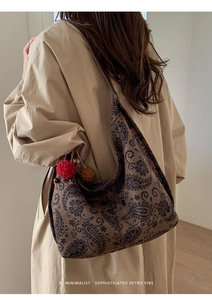 Retro paisley tote bag with colorful pompom charms worn over a khaki trench coat