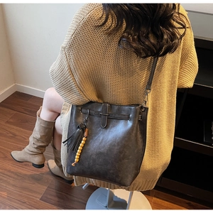 Détail du sac seau en cuir marron avec pompons porté par un mannequin en intérieur