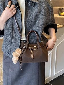 Mini sac seau marron foncé avec breloque ours et sangle montré sur manteau tweed
