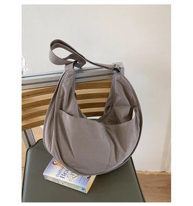 Detail of taupe nylon crescent bag showing smooth fabric texture on a wooden chair