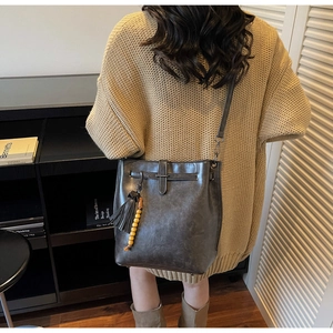 Détail d'un sac seau en cuir gris foncé avec boucle en métal et breloque à pompon décoratif
