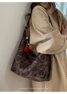 Detail view of a retro dark brown paisley tote bag with red and khaki knitted pom-poms