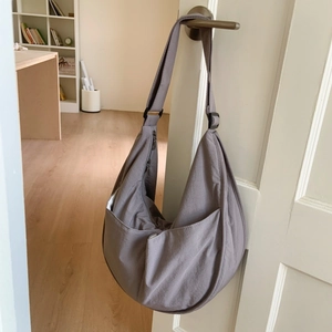 Detailed side view of a large mauve nylon crescent bag hanging on a white door handle