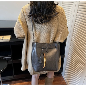 Détail du sac seau gris vintage avec glands en cuir et perles en bois sur un pull en tricot beige