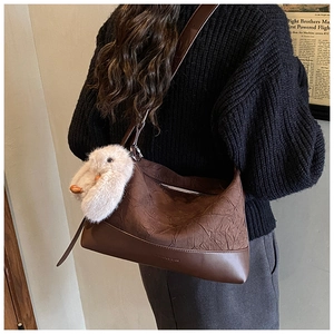 Detail view of a brown pleated suede shoulder bag with a cute plush duck charm