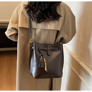 Détail du sac seau en cuir marron foncé avec boucle décorative et pompon perlé amovible
