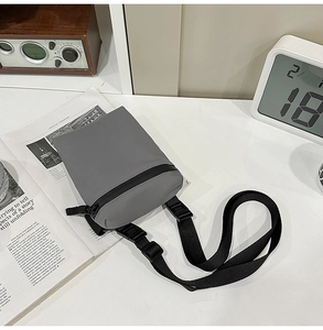 Minimalist grey nylon crossbody bag with adjustable strap on a lifestyle workspace desk