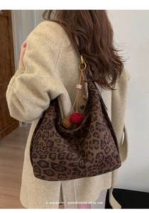Detailed close-up of a leopard print hobo bag with red pompom charms on a model