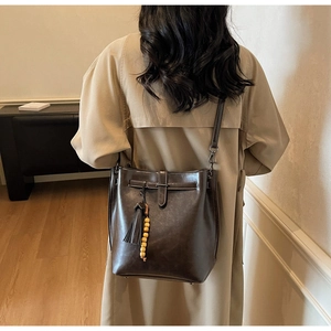 Détail du sac seau marron foncé avec pendentif à pompon et bandoulière sur trench-coat