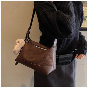 Detail of dark brown pleated crossbody bag featuring a cute white plush duck charm