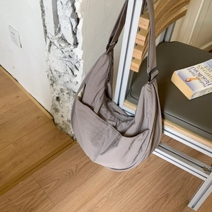 Detail of adjustable black buckle on a taupe nylon crescent shoulder bag shown on a chair