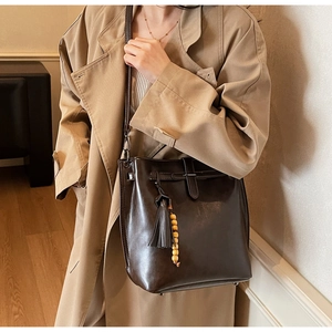 Détail du sac seau en cuir marron foncé avec pompon élégant et perles en bois