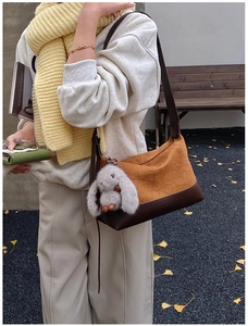Detail of pleated mustard yellow shoulder bag with a plush bunny charm on a wooden bench