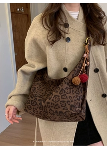 Detailed view of leopard print canvas tote bag with plush charms on a beige coat
