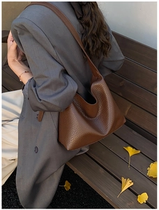 Brown lychee leather hobo bag worn on shoulder by model in an outdoor fall setting