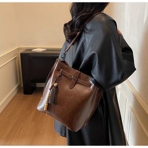 Détail d'un sac seau vintage en cuir marron foncé avec pompon et perles en bois