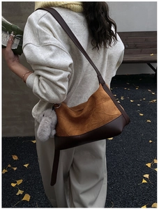 Detail view of a pleated hobo bag with leather stitching and a plush rabbit charm