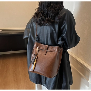 Détail d'un sac seau en cuir caramel avec pampille à franges et breloque en perles de bois