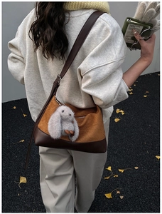 Detail of a brown pleated crossbody bag with a cute rabbit plush charm in an autumn scene