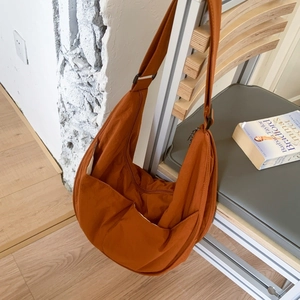 Burnt orange crescent nylon crossbody bag with wide strap hanging on wooden chair