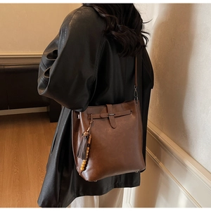 Détail du sac seau en cuir marron vintage avec pompon et breloque en bois ronde