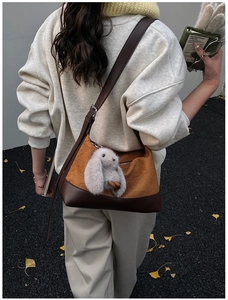 Detail of a brown leather shoulder bag with a cute white bunny charm and autumn leaf background