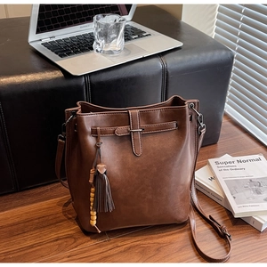 Détail d'un sac seau en cuir marron avec pompon et perles en bois sur un sol en bois