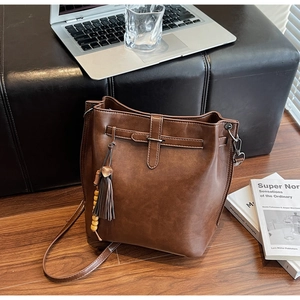 Détail du sac seau marron caramel avec pompon et perles en bois sur sol en bois