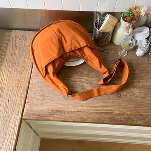 Detailed top view of a burnt orange nylon crescent crossbody bag on a wooden surface