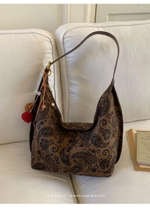 Detail of retro paisley print tote bag with brown pompom and beaded charm on white sofa